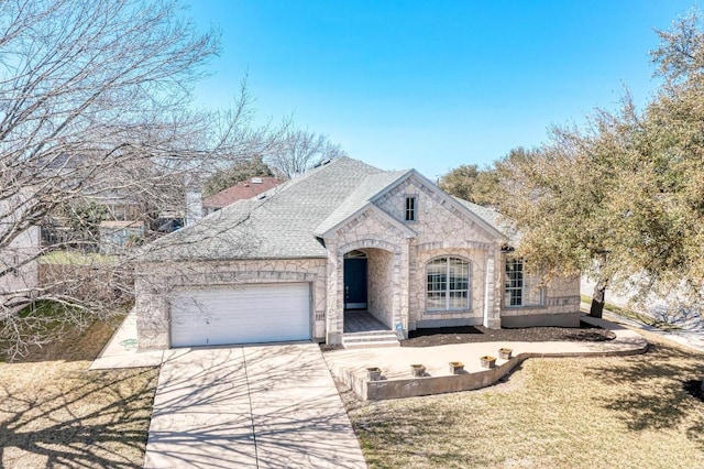 french country style house with concrete driveway, an attached garage, stone siding, and roof with shingles