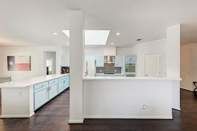 1000 Rutgers Dr, Pflugerville, TX 78660 - kitchen featuring freestanding refrigerator, a peninsula, wall chimney range hood, dark wood finished floors, and a skylight