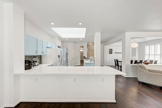 kitchen with blue cabinetry, white fridge with ice dispenser, a peninsula, a skylight, and light countertops