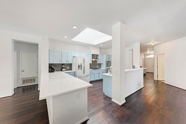 kitchen with a peninsula, wall chimney range hood, white refrigerator with ice dispenser, and a skylight