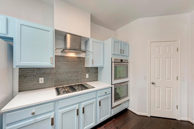 kitchen with double wall oven, dark wood-style flooring, stainless steel gas stovetop, wall chimney range hood, and backsplash