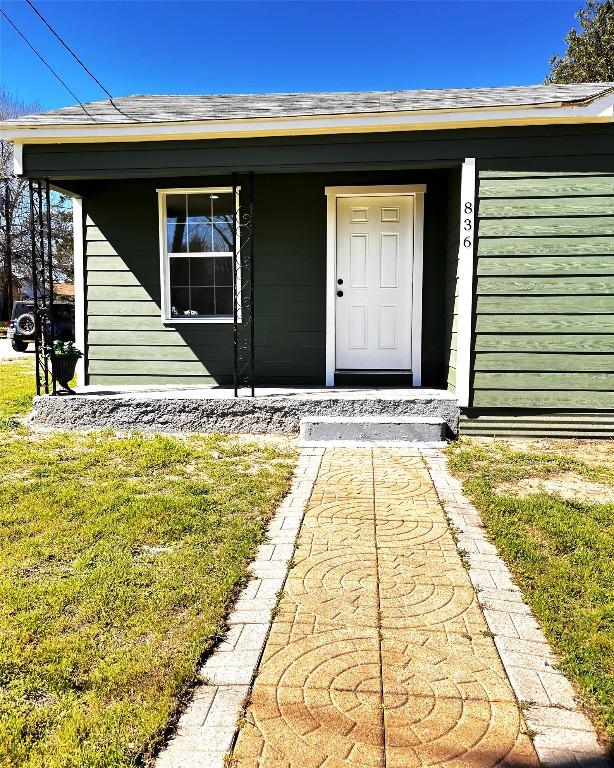 view of exterior entry with a porch, a shingled roof, and a yard