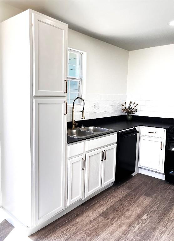 kitchen featuring dark wood-style floors, white cabinetry, a sink, dishwasher, and dark countertops