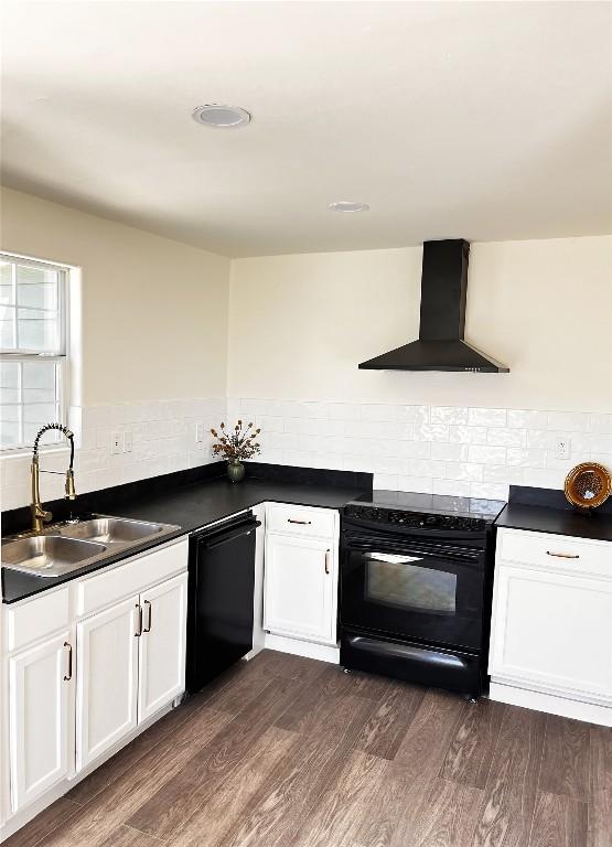 kitchen with dark countertops, wall chimney range hood, dark wood-style floors, black appliances, and a sink