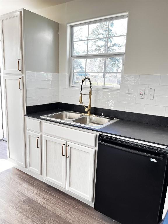 kitchen with dark countertops, white cabinets, black dishwasher, and a sink