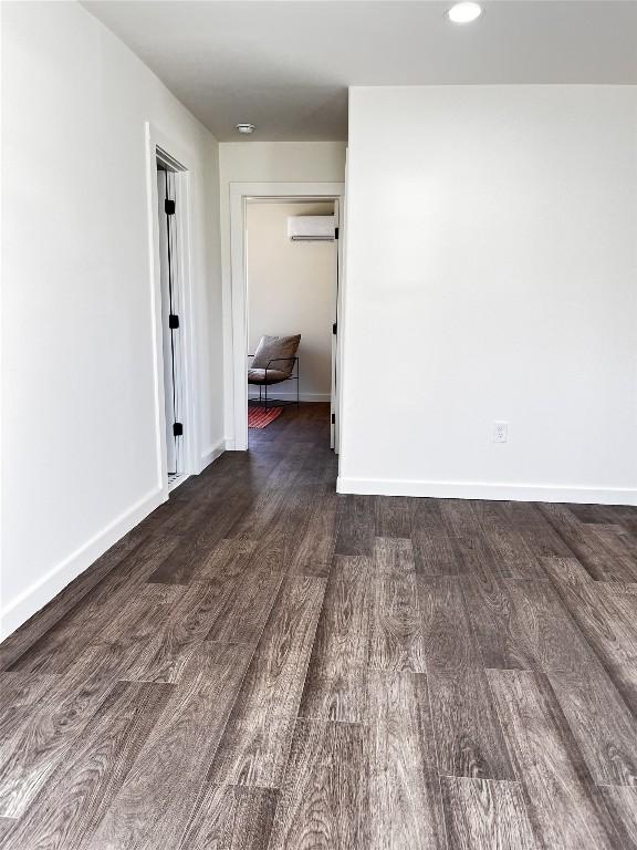 spare room featuring a wall mounted AC, baseboards, and wood finished floors