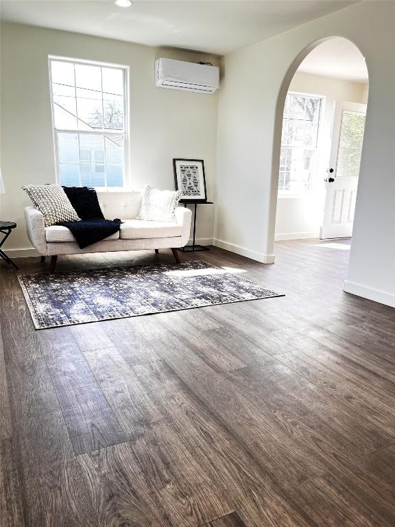 unfurnished room featuring wood finished floors, arched walkways, a wall mounted air conditioner, and baseboards