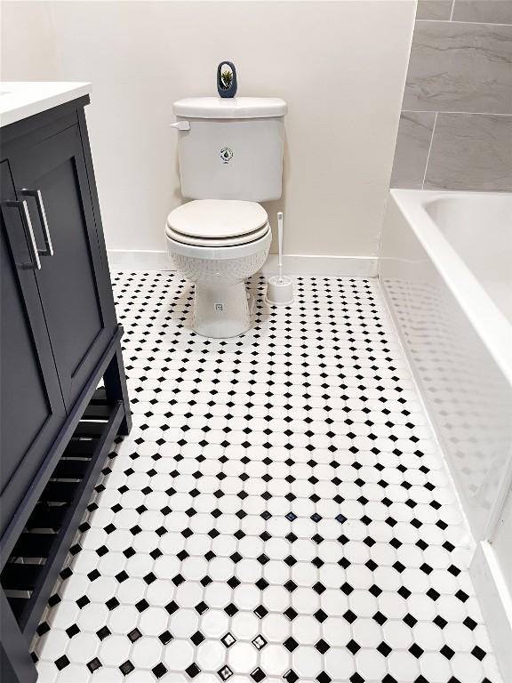 bathroom featuring tile patterned floors, baseboards, toilet, and a bath