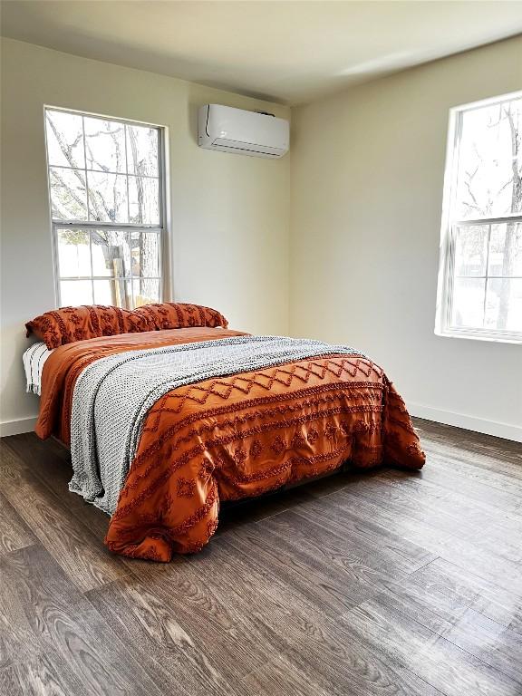 bedroom featuring baseboards, wood finished floors, and a wall unit AC