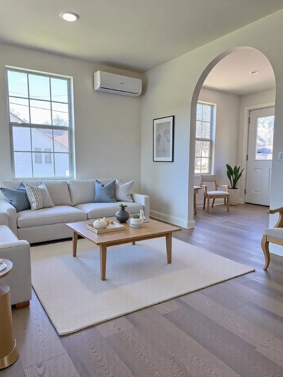 living area with a wall mounted air conditioner, wood finished floors, recessed lighting, arched walkways, and baseboards