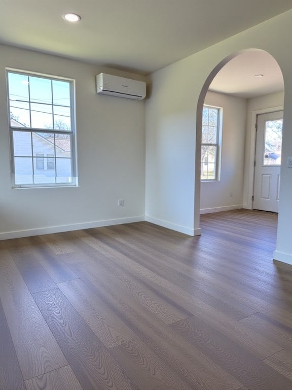 unfurnished room with baseboards, arched walkways, dark wood finished floors, and a wall unit AC