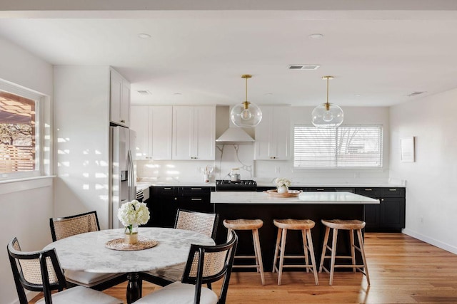 kitchen featuring dark cabinetry, visible vents, stainless steel fridge with ice dispenser, wall chimney exhaust hood, and a center island