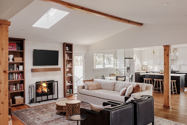 living area featuring vaulted ceiling with beams, light wood-style floors, and a lit fireplace