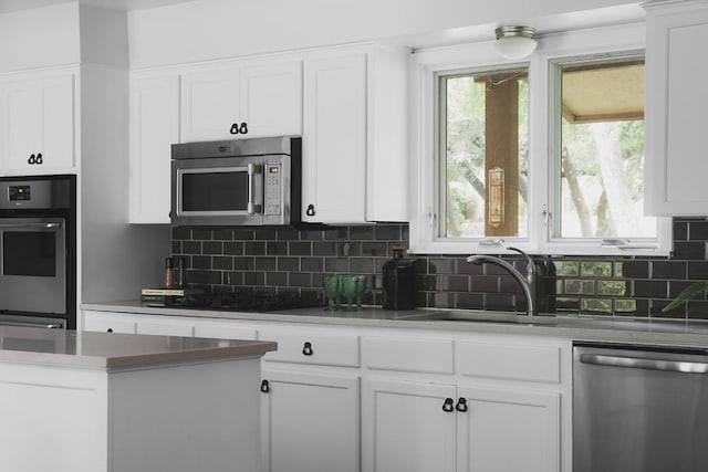 kitchen featuring backsplash, white cabinets, stainless steel appliances, and a sink