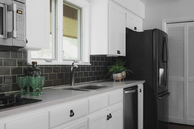 kitchen with a sink, light countertops, appliances with stainless steel finishes, white cabinetry, and backsplash