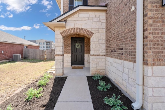 property entrance with central air condition unit, fence, brick siding, and stone siding