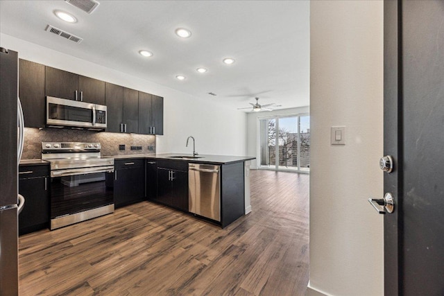 kitchen with visible vents, a sink, appliances with stainless steel finishes, decorative backsplash, and dark wood-style flooring