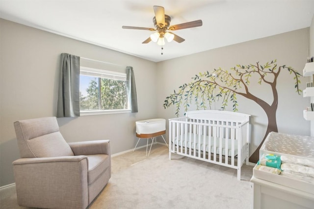 carpeted bedroom with ceiling fan, baseboards, and a nursery area