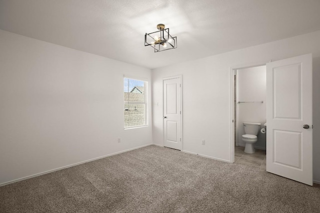 unfurnished bedroom with carpet floors, baseboards, and ensuite bathroom