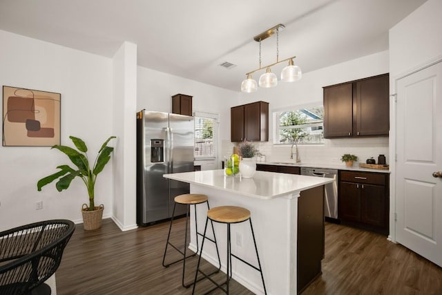 kitchen featuring dark brown cabinetry, a breakfast bar, a sink, stainless steel appliances, and visible vents