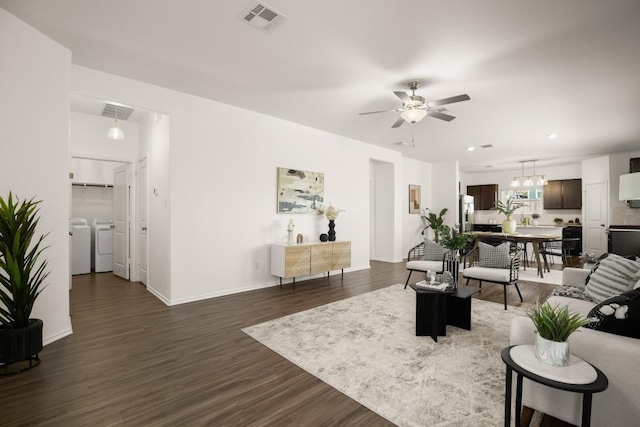 living room featuring visible vents, dark wood-style flooring, washing machine and dryer, baseboards, and ceiling fan with notable chandelier