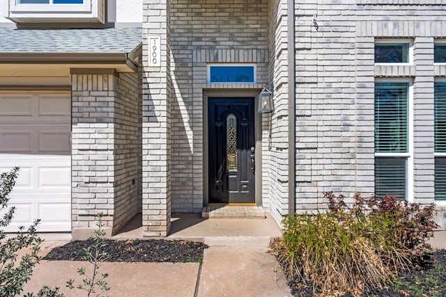 doorway to property with brick siding, an attached garage, and a shingled roof