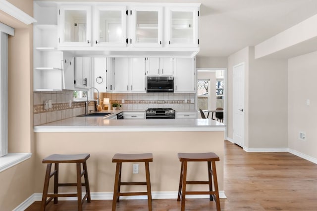 kitchen featuring open shelves, a sink, light countertops, black range with gas stovetop, and stainless steel microwave