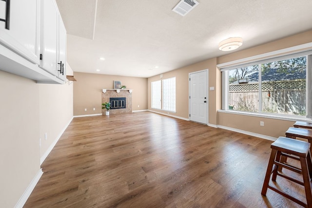 unfurnished living room featuring a tiled fireplace, visible vents, plenty of natural light, and wood finished floors