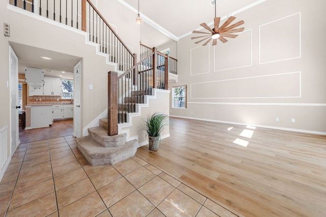 foyer entrance featuring ornamental molding, stairway, a high ceiling, light tile patterned flooring, and ceiling fan