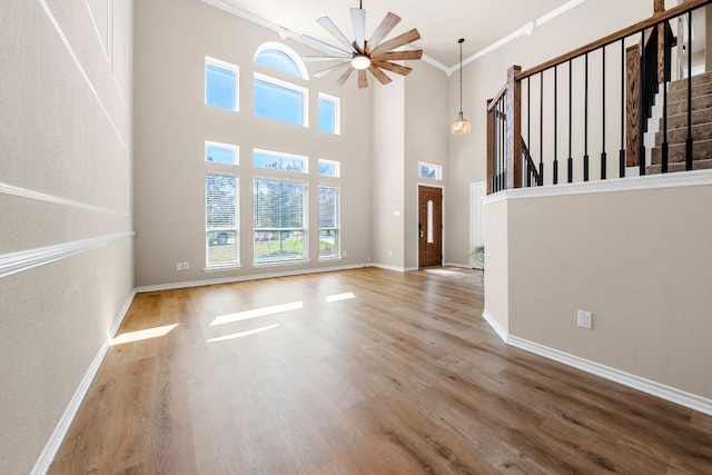 unfurnished living room featuring stairway, crown molding, baseboards, and wood finished floors