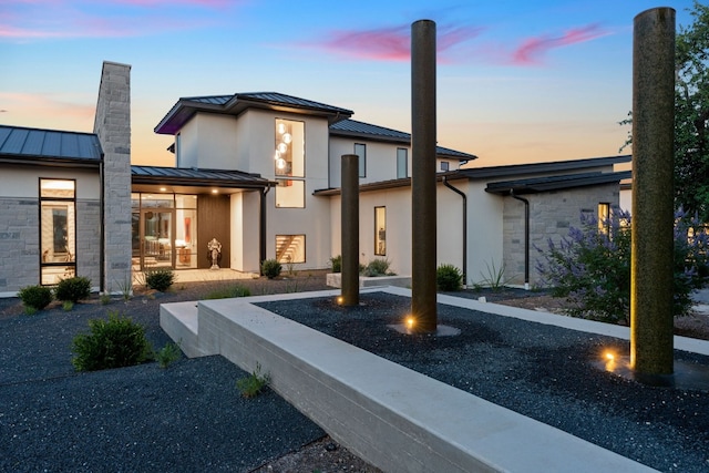 back of property at dusk featuring a standing seam roof, stone siding, and metal roof