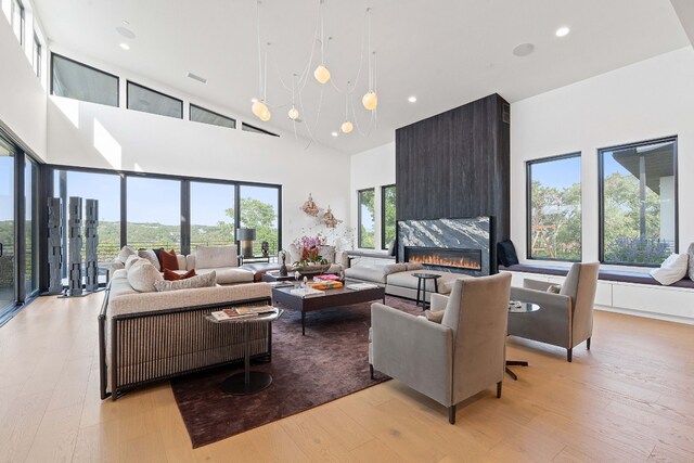 living area featuring a fireplace, light wood-style floors, recessed lighting, and a high ceiling