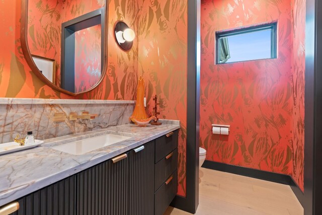 bathroom featuring toilet, wallpapered walls, vanity, and wood finished floors