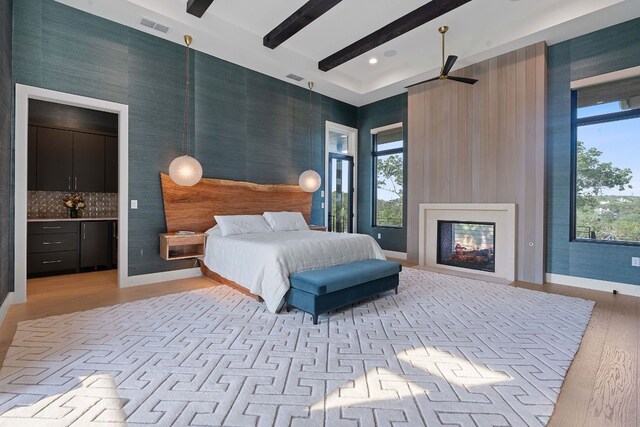 bedroom featuring visible vents, beam ceiling, a multi sided fireplace, light wood finished floors, and baseboards