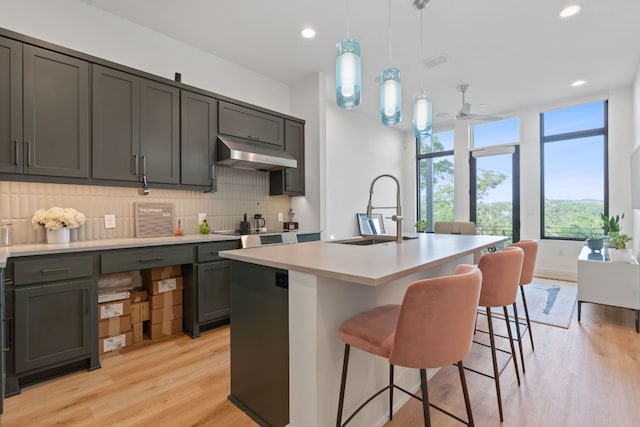 kitchen with under cabinet range hood, a sink, tasteful backsplash, light wood finished floors, and light countertops