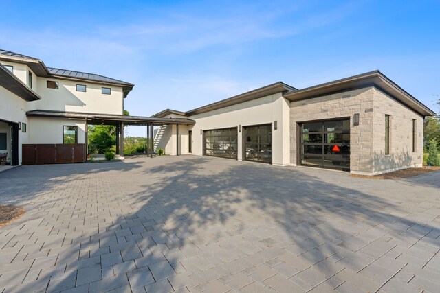 exterior space with a standing seam roof, a garage, stone siding, decorative driveway, and metal roof