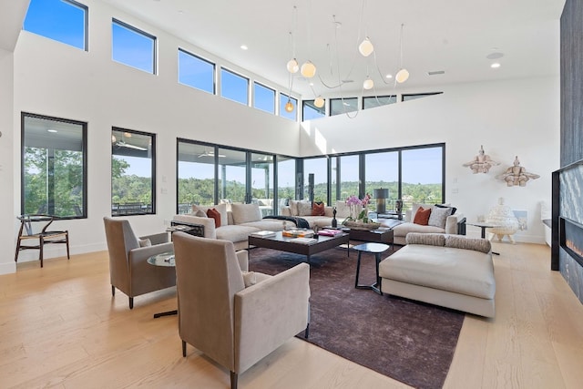 living room featuring light wood-type flooring, recessed lighting, a large fireplace, a high ceiling, and baseboards