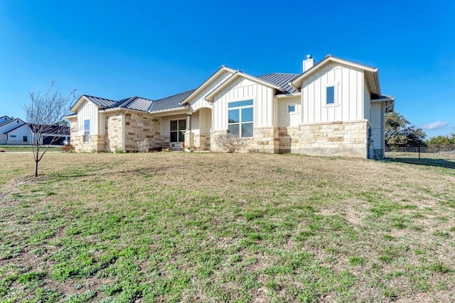 view of front of house featuring metal roof, board and batten siding, a front lawn, and stone siding