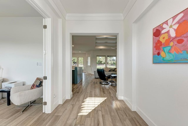 corridor featuring baseboards, crown molding, and light wood-style flooring