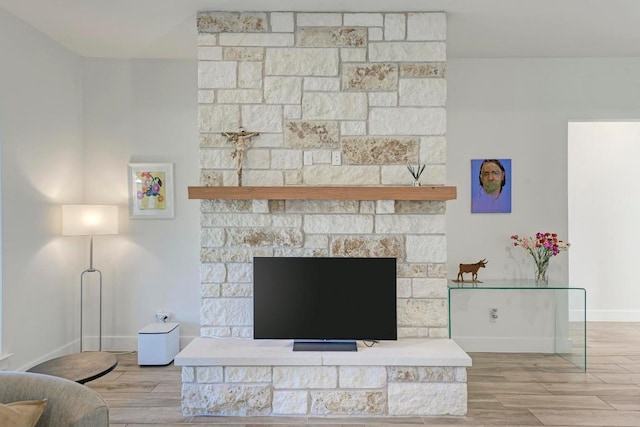 living room featuring a stone fireplace, wood finished floors, and baseboards