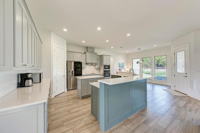 kitchen featuring decorative backsplash, light wood-style floors, appliances with stainless steel finishes, light countertops, and a large island