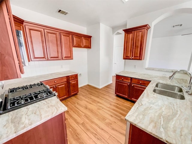 3128 Flinders Reef Ln, Austin, TX 78728 - kitchen featuring arched walkways, light wood finished floors, light stone counters, and reddish brown cabinets