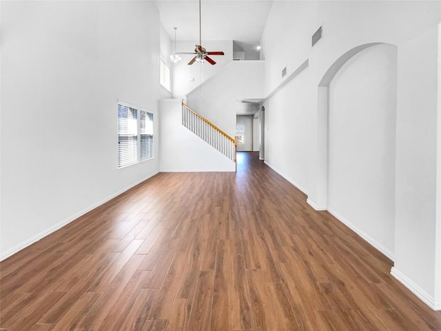 3128 Flinders Reef Ln, Austin, TX 78728 - unfurnished living room with a ceiling fan, wood finished floors, stairs, a towering ceiling, and arched walkways