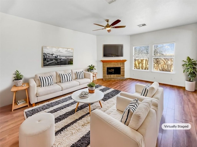 living area featuring a ceiling fan, a brick fireplace, wood finished floors, and visible vents