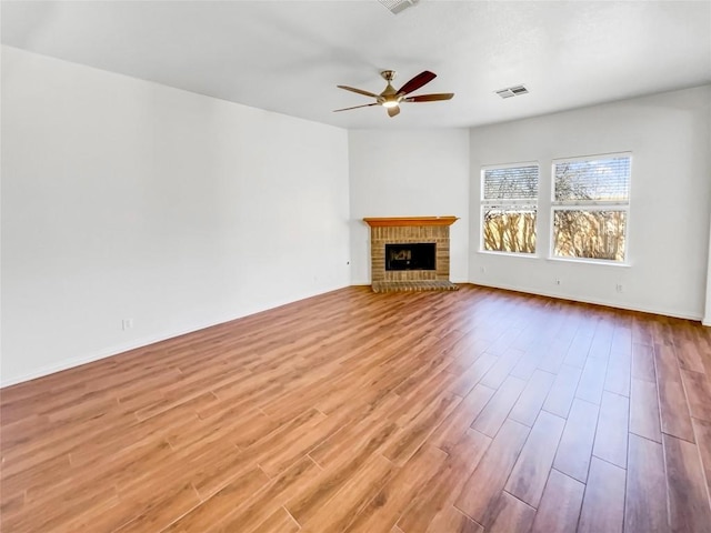 unfurnished living room with wood finished floors, baseboards, visible vents, a fireplace, and ceiling fan