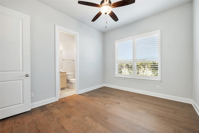 unfurnished bedroom featuring baseboards, ensuite bath, dark wood-style floors, and a ceiling fan