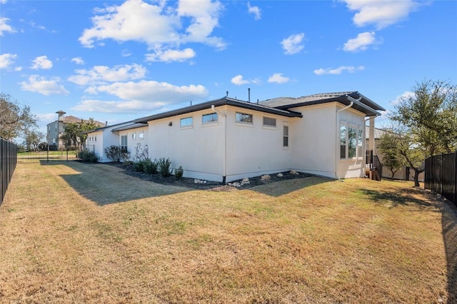 back of house with stucco siding, a yard, and fence