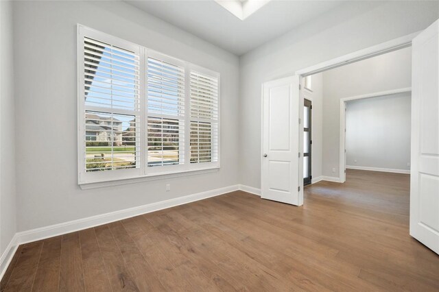 unfurnished room with a skylight, baseboards, and wood finished floors