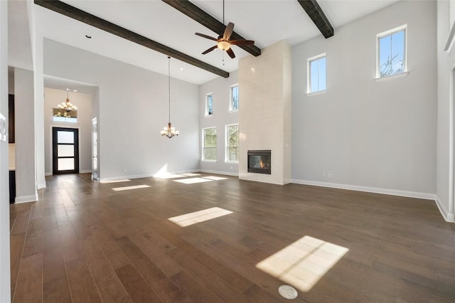 unfurnished living room with baseboards, a tile fireplace, dark wood-type flooring, a towering ceiling, and beamed ceiling