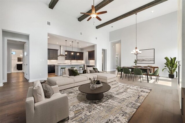 living room with visible vents, dark wood-type flooring, baseboards, beam ceiling, and ceiling fan with notable chandelier